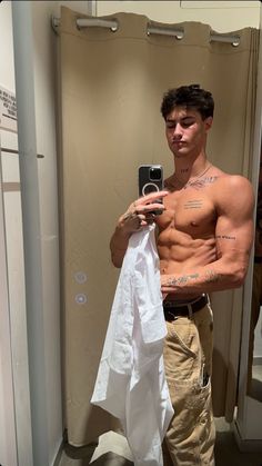 a shirtless man taking a selfie in the mirror with his cell phone and towel