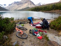 two mountain bikers preparing their gear on the side of a lake