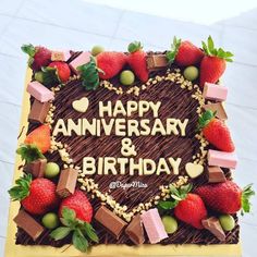 a heart shaped cake with strawberries and chocolates on the top that says happy anniversary & birthday