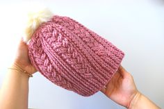 a hand holding a pink knitted hat with a white pom - pom