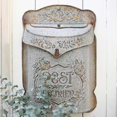 an old metal post box sitting on the side of a white wall next to a potted plant