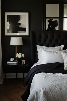 a bedroom with black walls and white bedding, framed pictures above the headboard