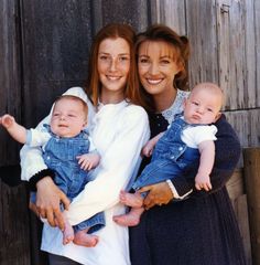 two women and one baby are posing for a photo in front of a wooden fence