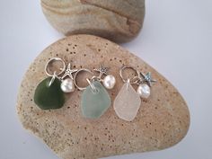 three sea glass charms sitting on top of a rock next to a starfish and seashell