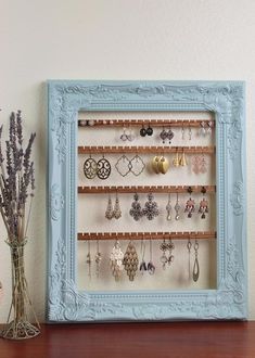 a blue frame holds earrings and earring hooks on a shelf next to a vase with dried lavenders