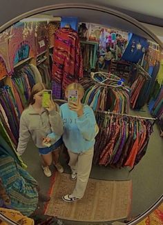 two women standing in front of a mirror looking at clothing on display and taking a selfie