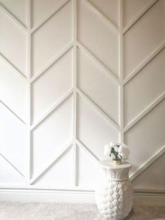 a white vase with flowers in it sitting on the floor next to a wall that has chevroned panels