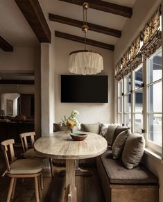 a room with a table, couch and television mounted to the wall next to a window