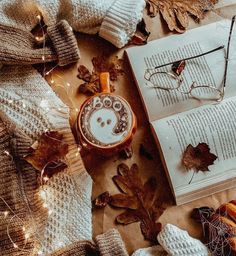 an open book and some glasses on top of a table with autumn leaves around it