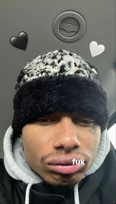 a man wearing a black and white hat with hearts on the wall behind him that says fuk