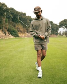 a man walking across a green covered golf course holding a golf club and wearing a hat