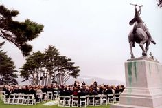 an outdoor ceremony with a statue of a man riding a horse and people sitting in chairs