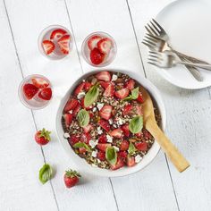 a bowl of strawberries and other fruit on a white wooden table with silverware