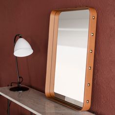 a mirror sitting on top of a wooden shelf next to a lamp and a table