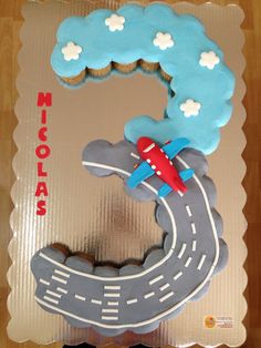 a cake shaped like the letter c with a plane on top and clouds in the sky