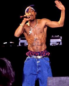 a shirtless man holding a microphone in his right hand and wearing blue jeans on stage