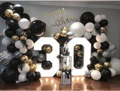 balloons and streamers decorate the backdrop for a 30th birthday party with black, gold and white balloons