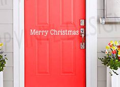 a red door with let it snow written on the side next to two white planters