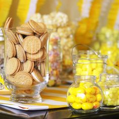 a table topped with glass vases filled with yellow and white candies covered in oreos