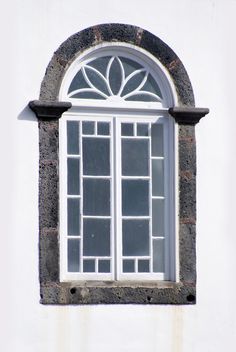 an arched window on the side of a white building with black trim and glass panes