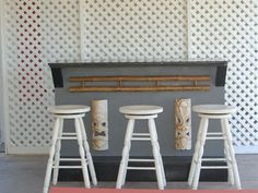 three white stools sitting next to each other in front of a wall with tiki masks on it