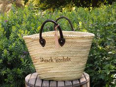 a large woven basket sitting on top of a wooden bench in front of some bushes