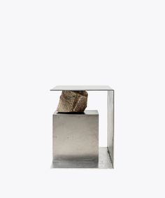 a rock sitting on top of a metal block in front of a white wall and floor