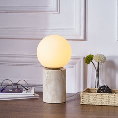 a white lamp sitting on top of a wooden table next to a basket filled with flowers