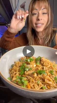 a woman holding a fork and spoon in front of a bowl of noodles with vegetables