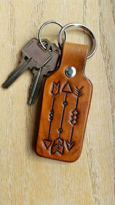 a leather keychain with an arrow design on it and two keys hanging from the front