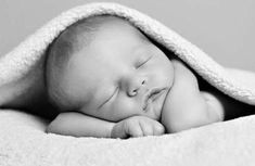 a black and white photo of a sleeping baby wrapped in a blanket with his eyes closed