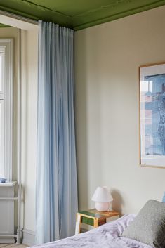 a bedroom with blue curtains and a bed in front of a painting on the wall