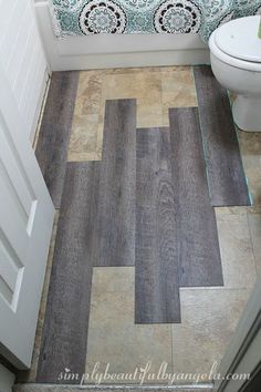 a white toilet sitting in a bathroom next to a wooden floor with tile on it