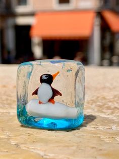 a penguin in a bottle sitting on top of a table next to a building and blue water