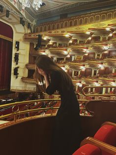 a woman standing in front of an auditorium talking on her cell phone while looking at the stage