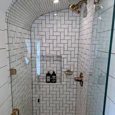 a white tiled bathroom with gold fixtures and glass shower door, along with toiletries on the wall