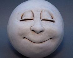 a white clay face with eyes closed on a gray surface, it appears to have been carved into the shape of a smiling face