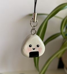 a glass bead with a smiling face hanging from a black cord next to a potted plant