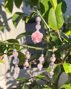 some pink beads hanging from a tree branch with a rose in the background and green leaves