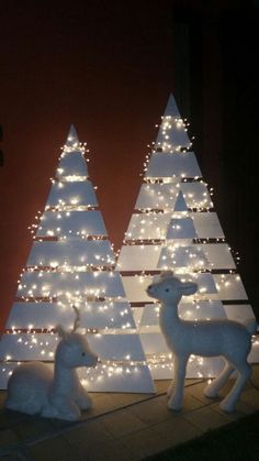 two white christmas trees decorated with lights and deer figurines in front of them