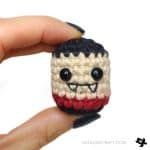 a hand holding a tiny doll with black eyes and red stripes on it's face