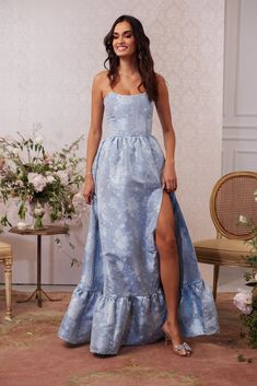 a woman in a blue dress standing next to a table with flowers and a chair