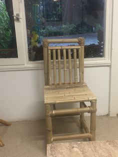 a wooden chair sitting in front of a window next to a stone slab on the ground