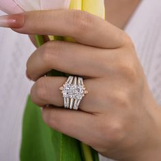 a close up of a person's hand holding a flower and two engagement rings