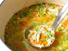 a ladle full of chicken noodle soup with peas and carrots