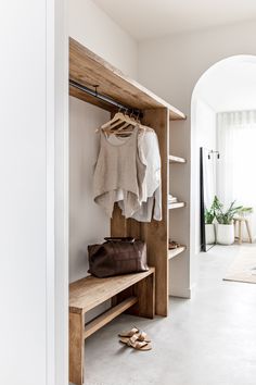 an open closet with clothes and shoes hanging on the wall, next to a wooden bench