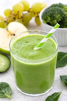 a green smoothie with a straw in it next to some fruit and veggies