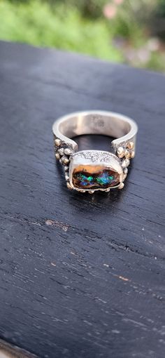 Cool, chunky and gender neutral ring with and bright offset Australian boulder opal. The opal is ethically sourced from Australia. This ring is handmade using sterling silver and has lots of 9ct gold balls snuggled around the setting. Size R.5 Boulder Opal Ring, Australian Boulder Opal, Chunky Rings, Funky Jewelry, Opal Ring, Boulder Opal, Opal Rings, Bouldering, Rings Statement