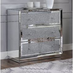 a mirrored cabinet with three drawers and two vases on top of the drawer, in front of a wall