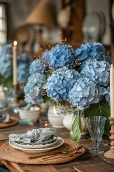 blue hydrangeas are in vases on the dining room table with candles and plates